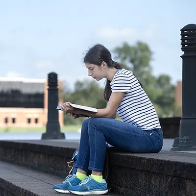 Female reading outdoors on steps by the lake.